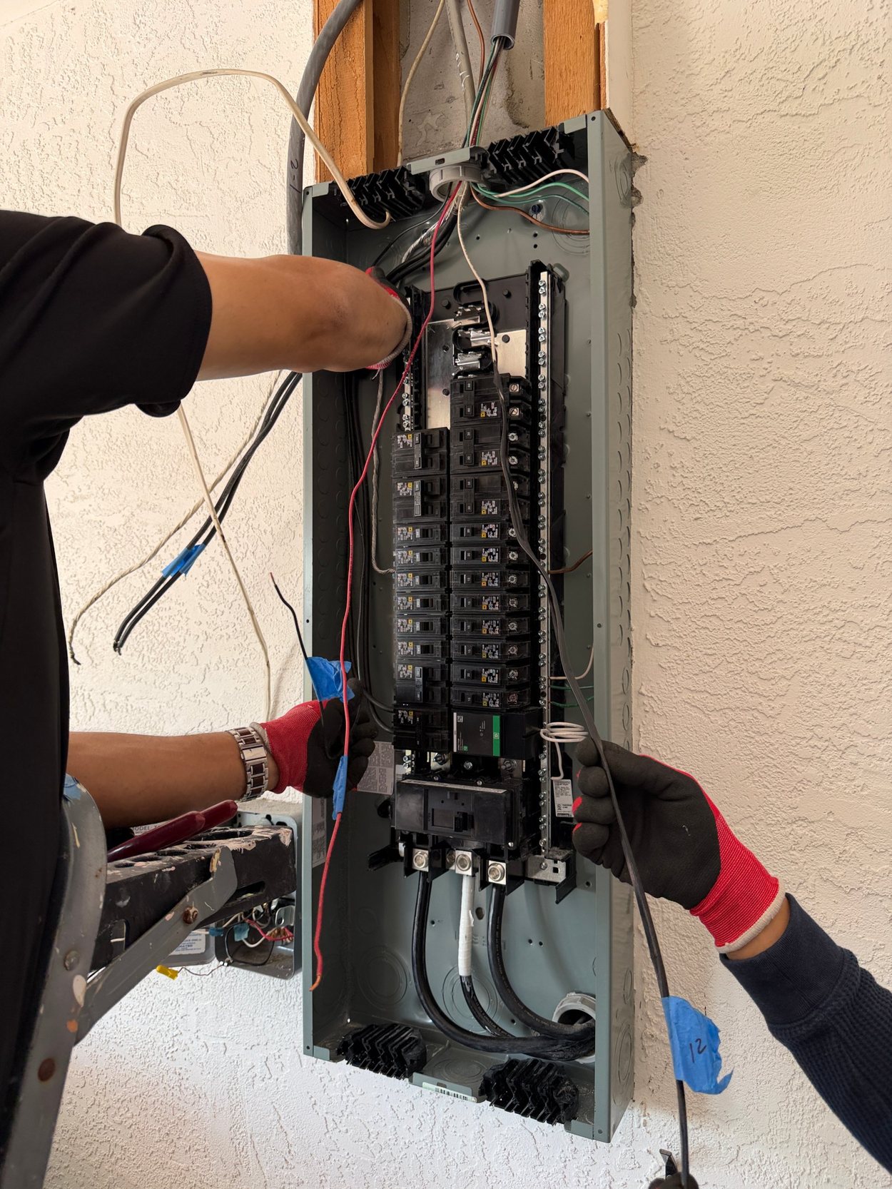 Two technicians wiring a new electrical panel, gloved hands pulling conductors into place.
